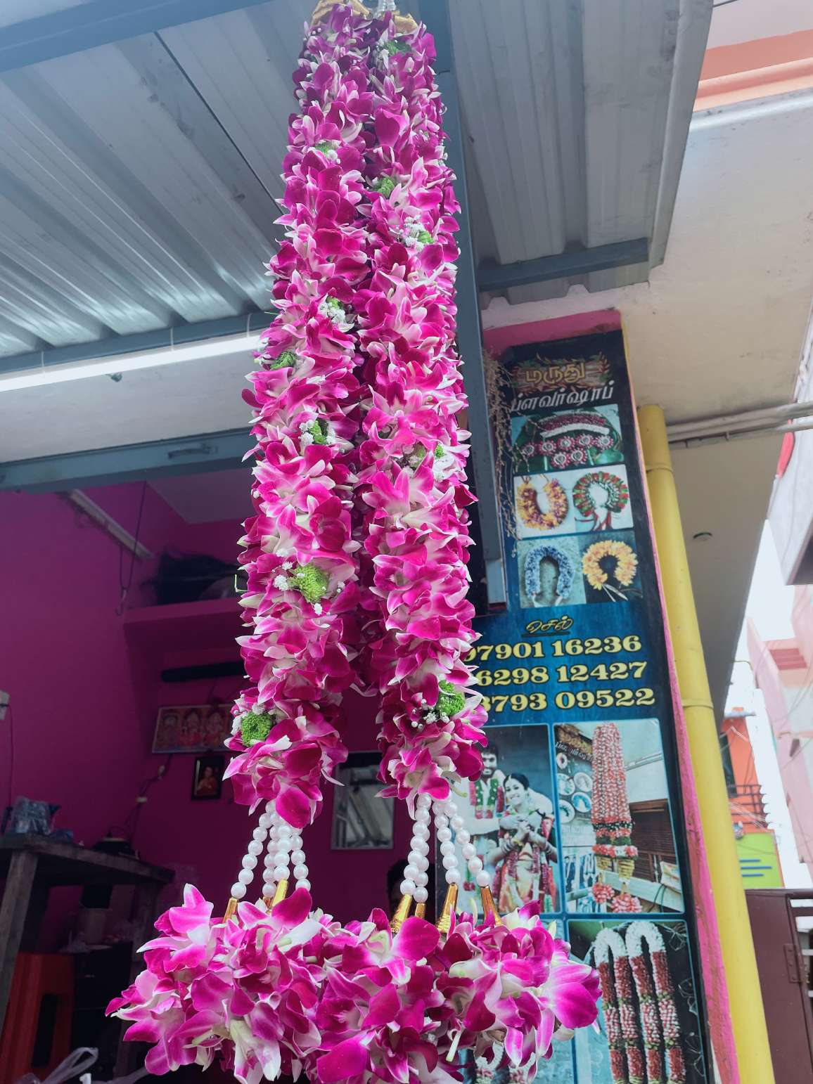 Magenta orchid garland with pearl strands and orchid tassels, hanging at a shop entrance.