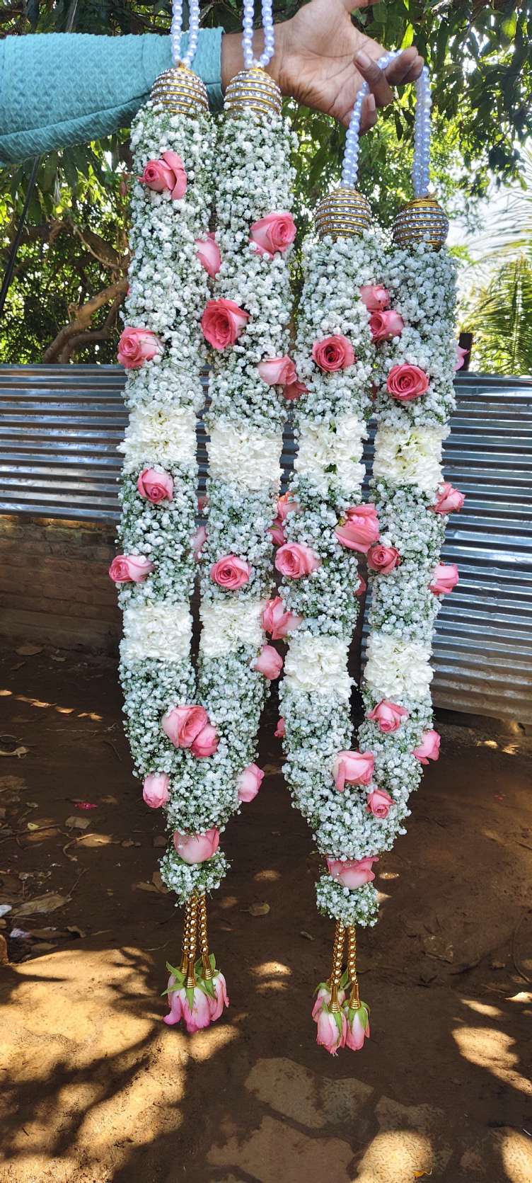 Pair of baby's breath garlands studded with pink roses, silver caps and gold bead tassels.