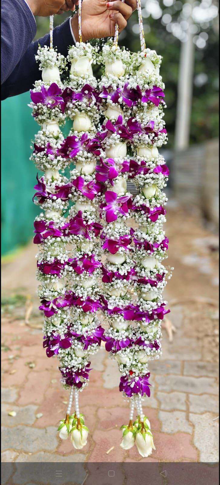 White floral garlands decorated with open purple flowers and pale rose tassels.