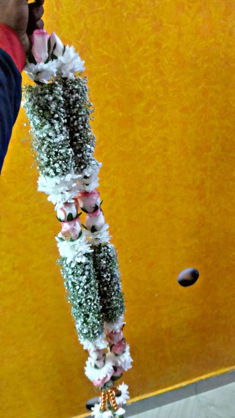 Garland of baby's breath sections with pink roses and white flower bands, held against a yellow wall.