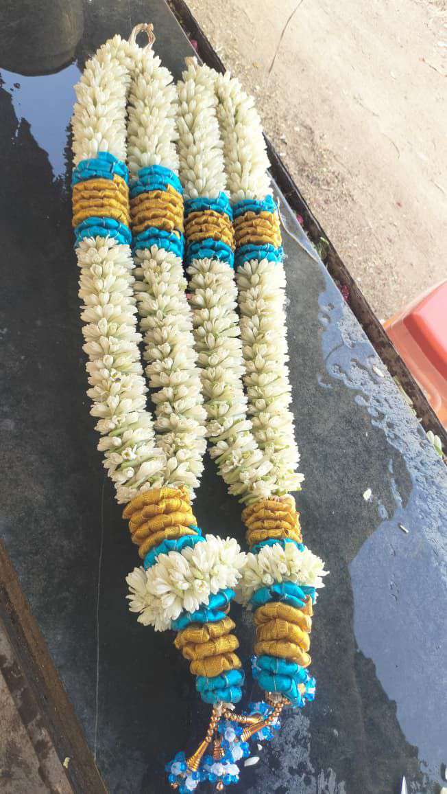 Pair of tuberose garlands with teal and gold bands near the top and at the tassels.