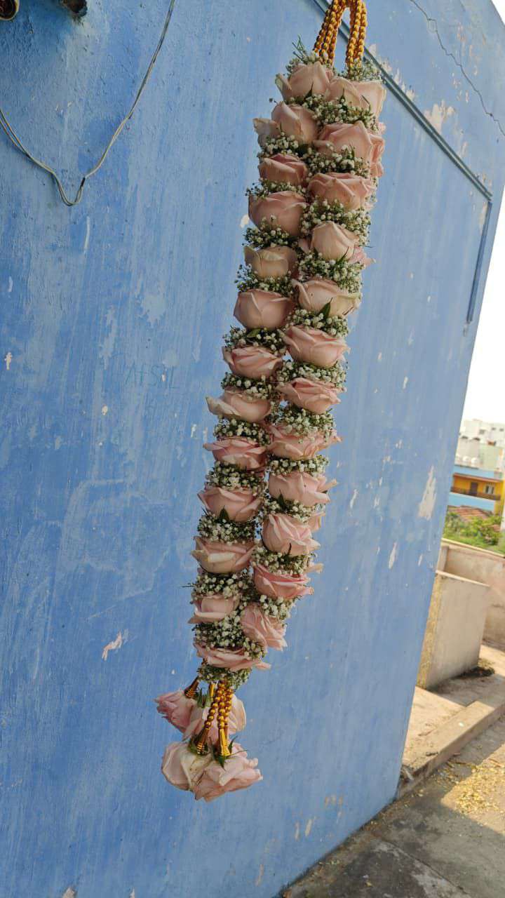 Single peach rose garland with green accents hanging against a blue wall, with a small tassel.