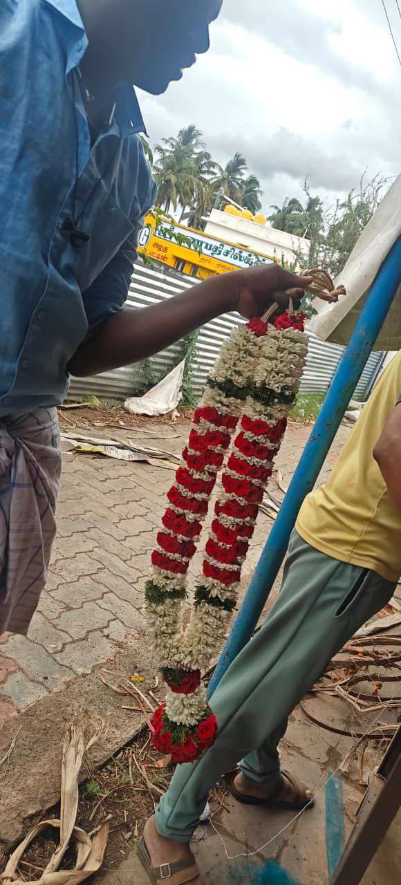 Red rose garland with ivory bands held up beside a road.