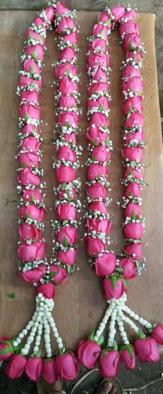 Two hot pink rose garlands with baby's breath, laid flat, with jasmine string tassels ending in pink roses.