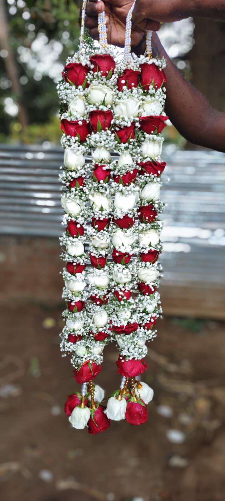 Hanging red and white rose garlands with white floral bands and mixed red and white tassels.