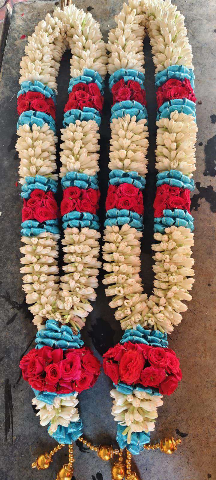 Pair of cream tuberose garlands with teal and red rose bands and red rose tassel balls, laid flat.