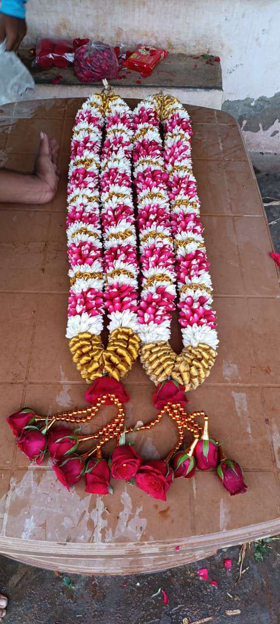 Tuberose and pink bud garland with a gold base and red rose tassels, laid on a table.