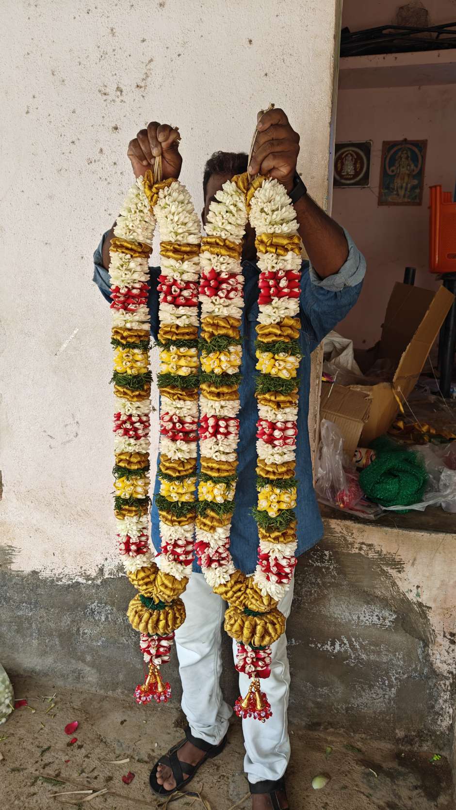 Pair of jasmine garlands striped in red, yellow and green, held up by a man.