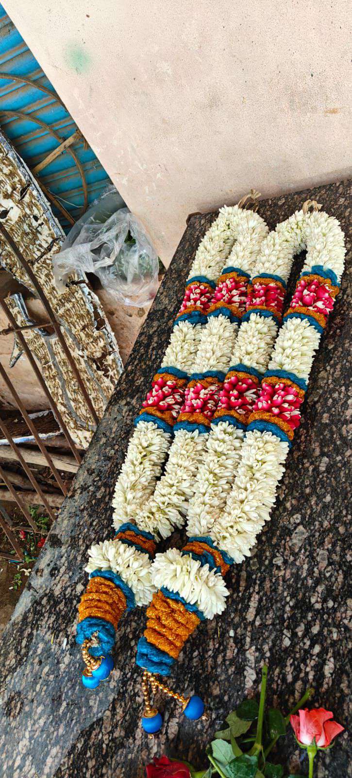 Tuberose garland with teal, pink and red bands and teal-and-gold tassels, photographed at an angle.
