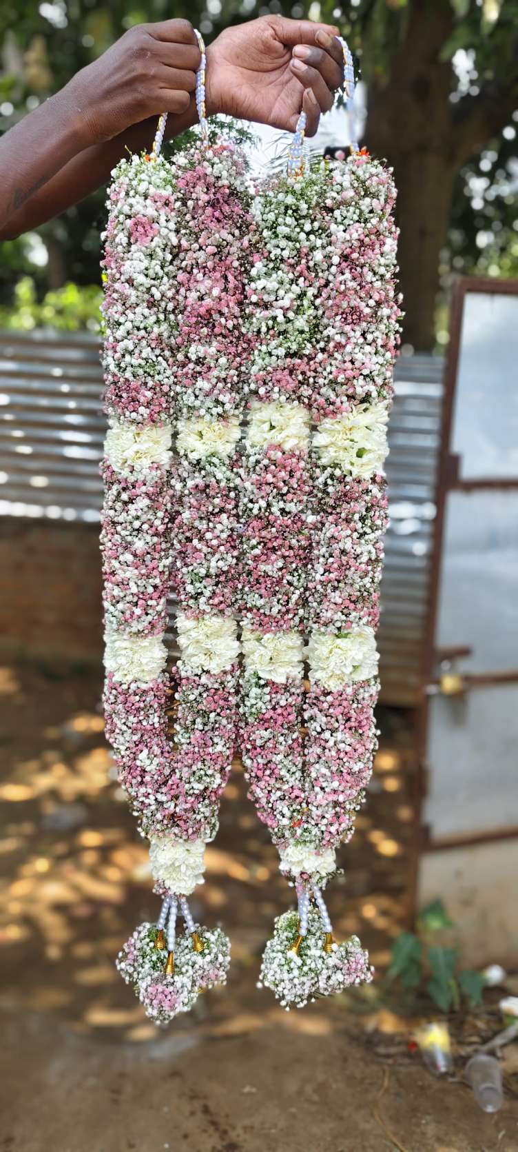 Dense blush and white floral garlands with broad white bands and rounded tassels.