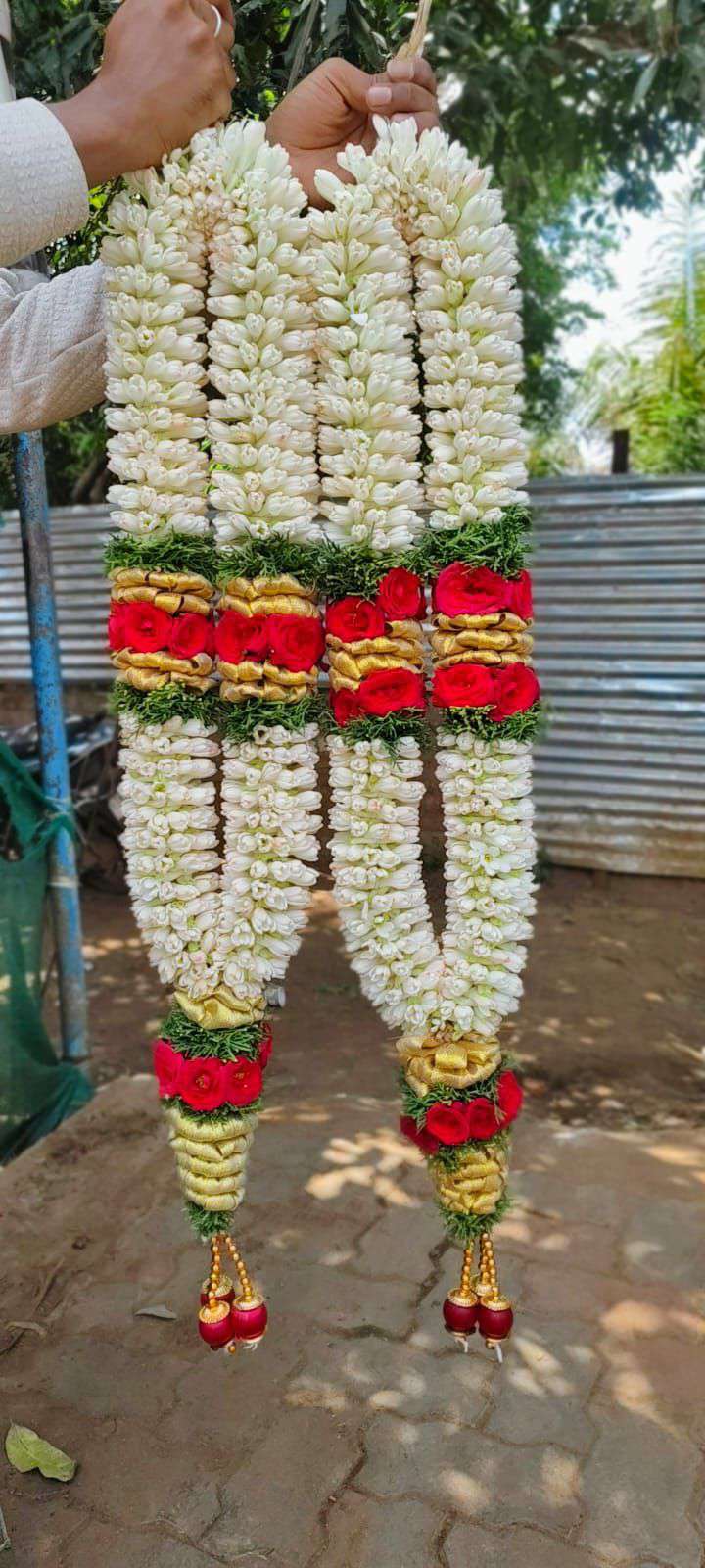 Pair of tuberose garlands with one red and gold band near the top and red and gold tassels.