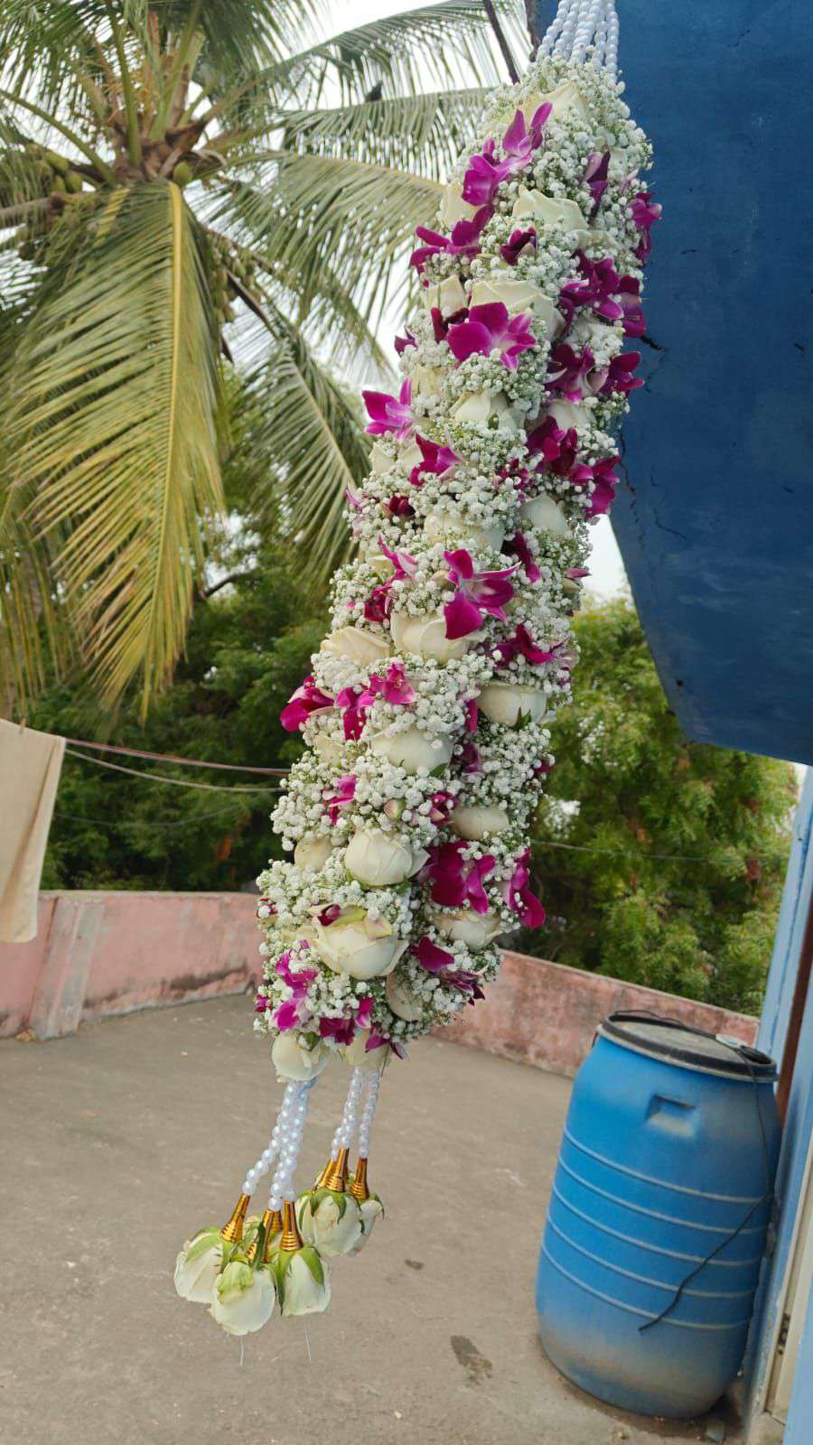 Hanging garland of white roses, purple orchids and baby's breath with white pearl strands and green bud tassels.