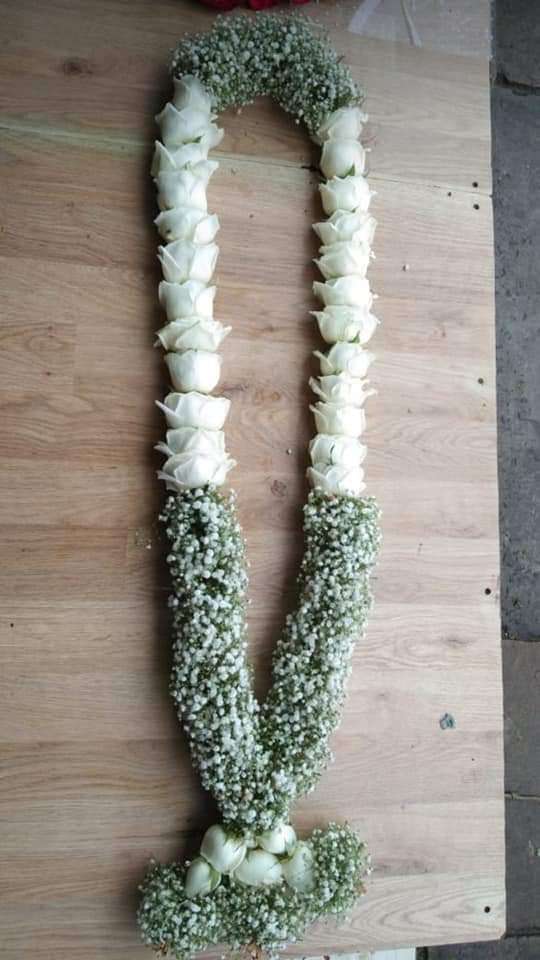 White rose garland with a baby's breath lower half and a white rose tassel, laid on wood.