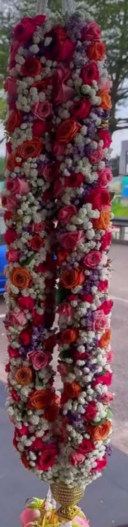Garland of red, pink, orange and white roses with baby's breath and purple accents, hanging outdoors.
