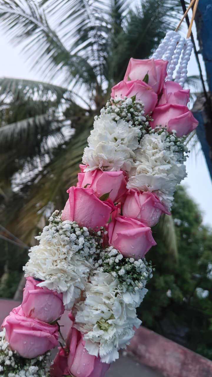 Close view of pink roses alternating with white carnations and baby's breath, with a white pearl hanger.