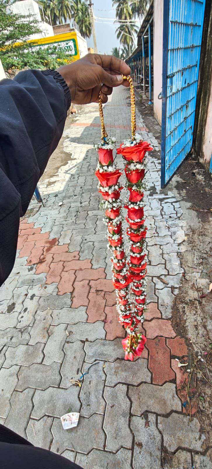 Narrow red rose garland with gold bead hangers, held up over a paved path.