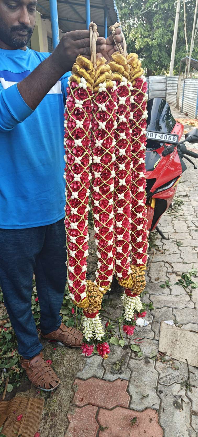 Red garland under a white lattice with gold tops and jasmine-cluster tassels, held by a man.