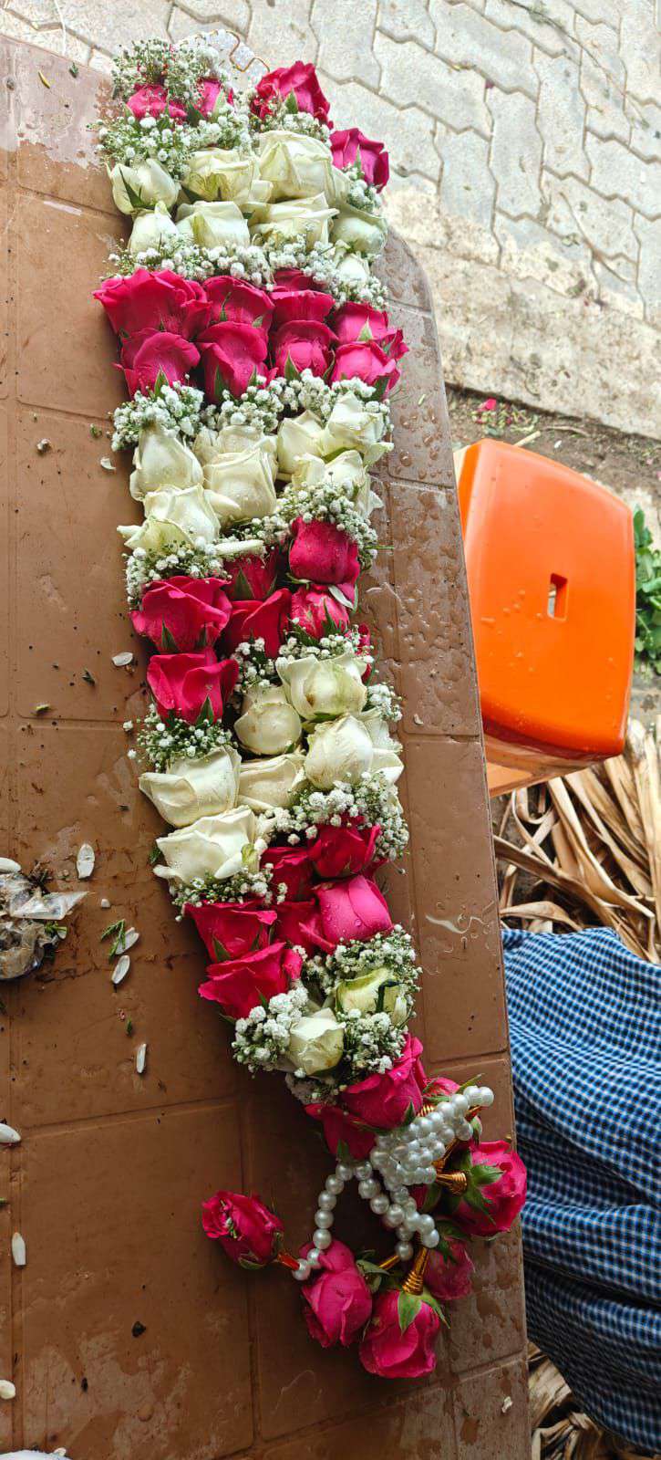Garland of red, pink and white rose sections with baby's breath, laid on a board with a pearl tassel.