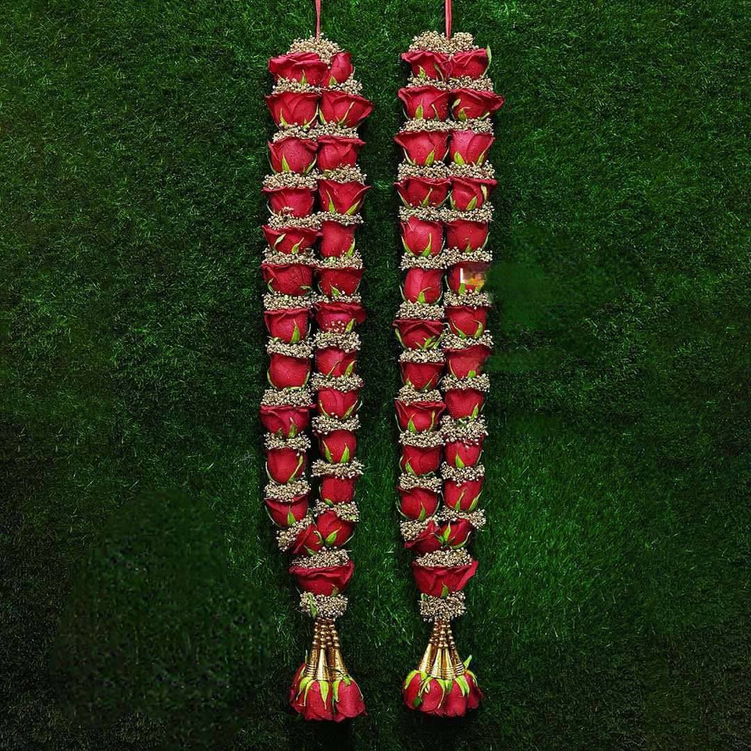 Red rose garlands with fine pale floral bands and gold-coloured tassel details on a dark green background.