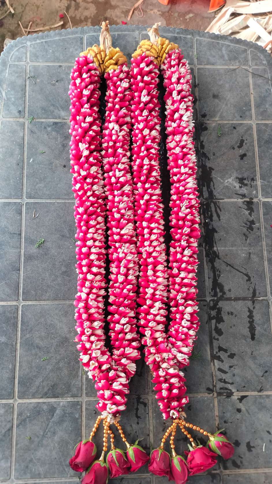 Pair of dense pink-and-white bud garlands with red rose tassels, laid on tiles.
