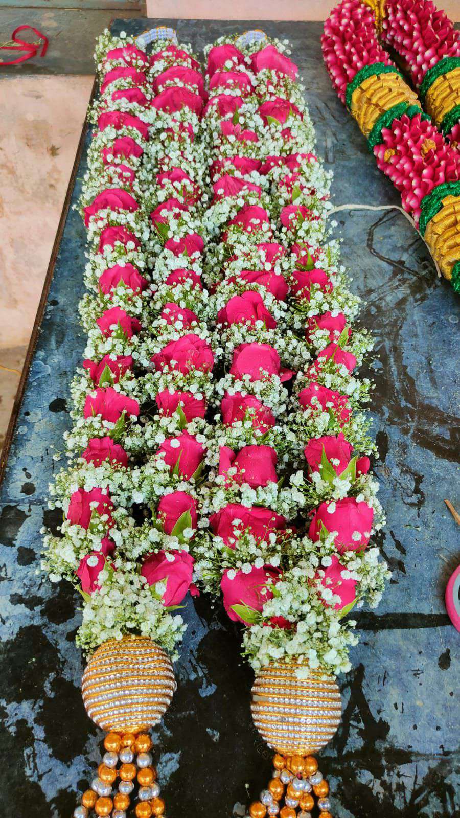 Two pink rose and baby's breath garlands laid flat, ending in gold-and-pearl ball tassels.