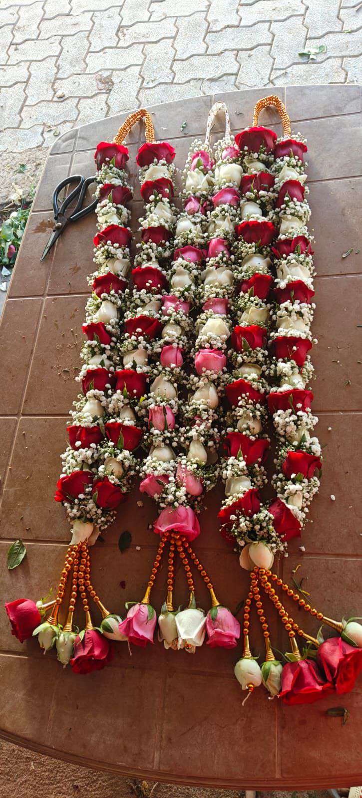 Two red, white and pink rose garlands laid on a table, with orange bead hangers and mixed rose tassels.