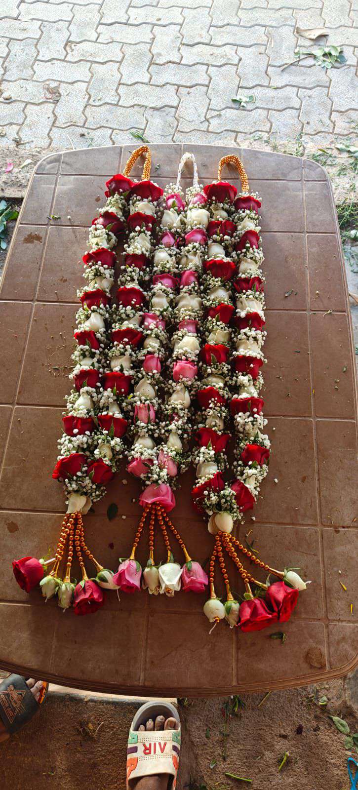 Two red and cream rose garlands laid on a table, with orange bead hangers and red rose tassels.