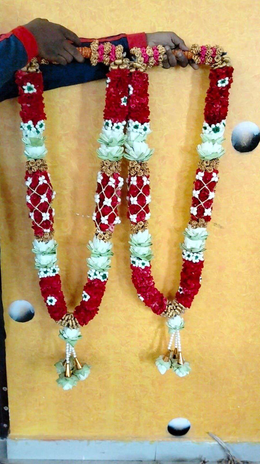 Pair of red lattice garlands with white rose sections and white tassels, against a yellow wall.