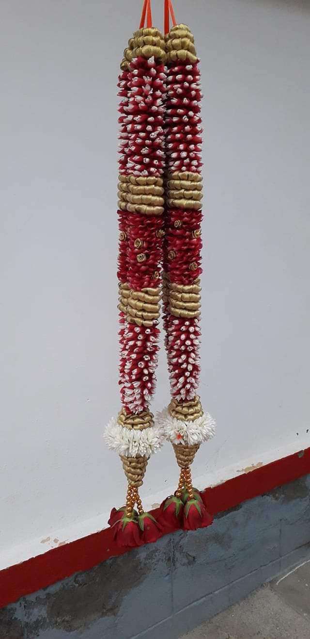 Pair of red-and-white bud garlands with gold bands and white frill tassels, hanging against a wall.