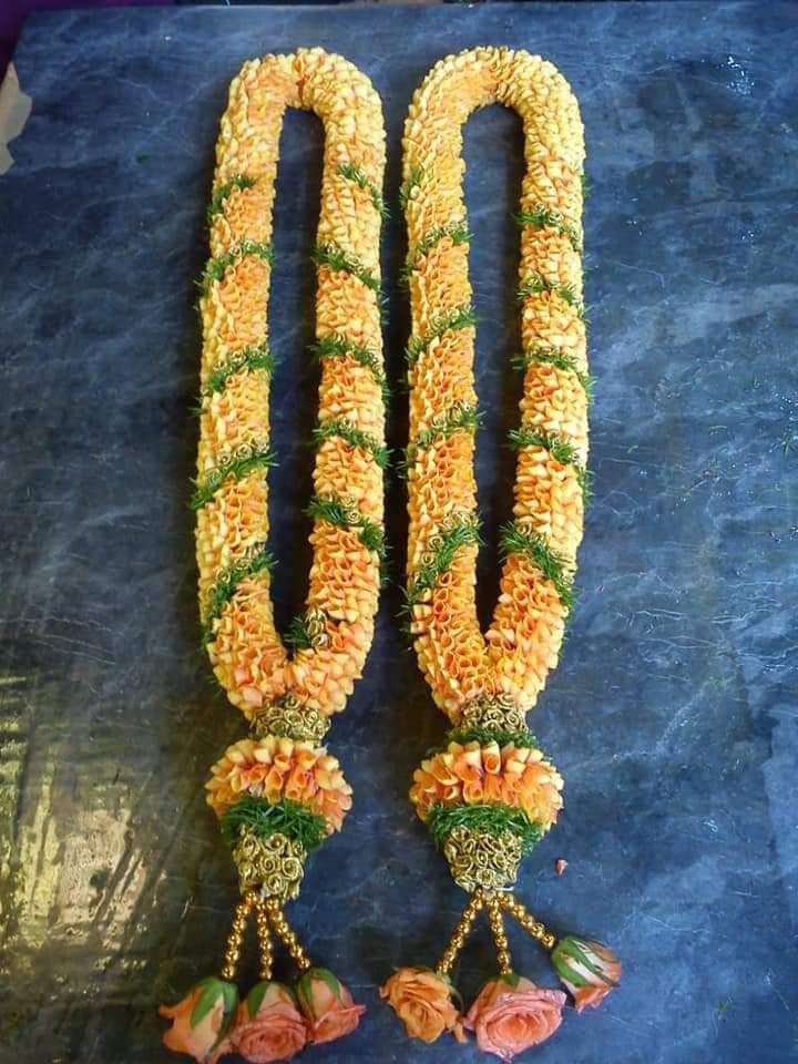 Golden yellow garlands with green floral separators and peach-coloured flower tassels on a blue surface.