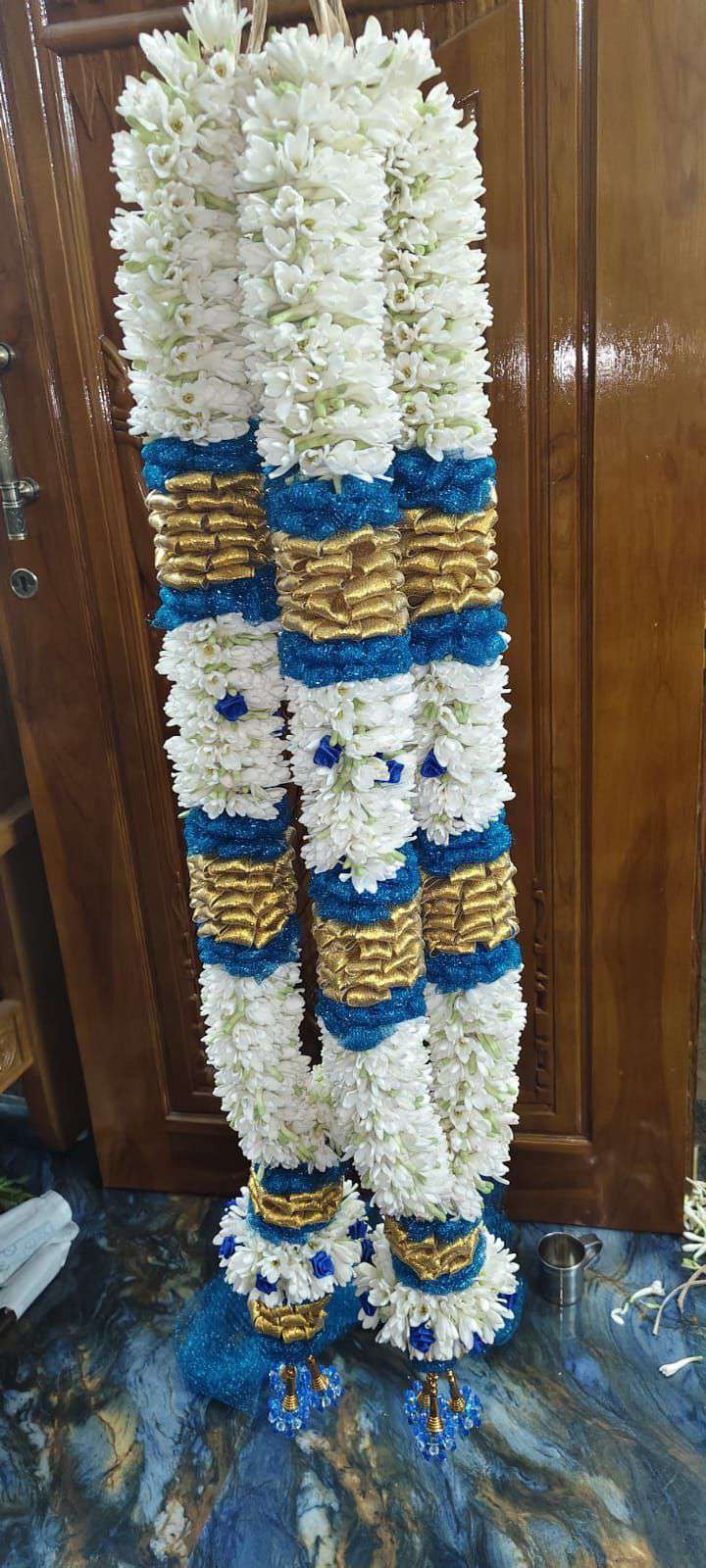 Tuberose garland with blue and gold bands and blue tassels, hanging against a wooden door.