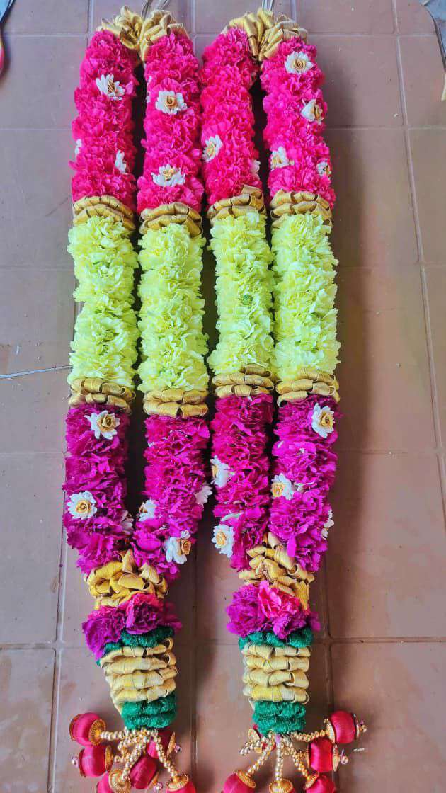 Pair of garlands in magenta and lime carnation sections with gold bands, laid on tiles.