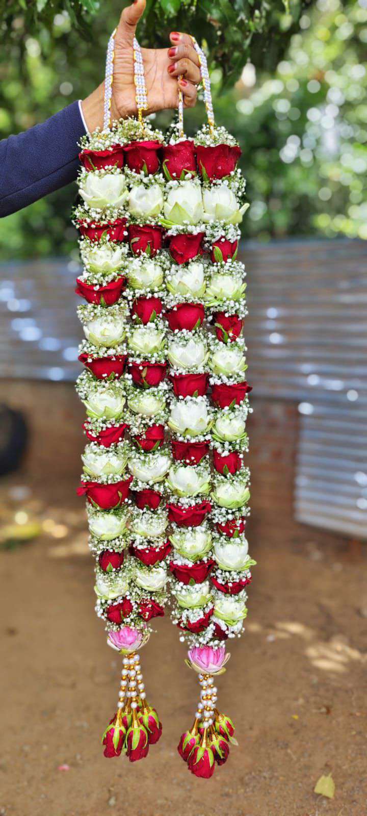 Pair of red and white rose garlands with baby's breath, pink lotus buds above pearl and gold tassels with red roses.