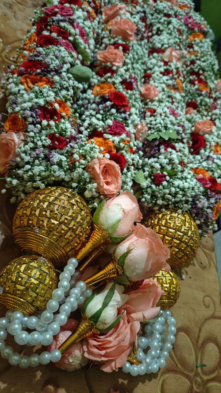 Baby's breath garland with red, orange and peach roses, gold ball caps and pearl strands, laid flat.