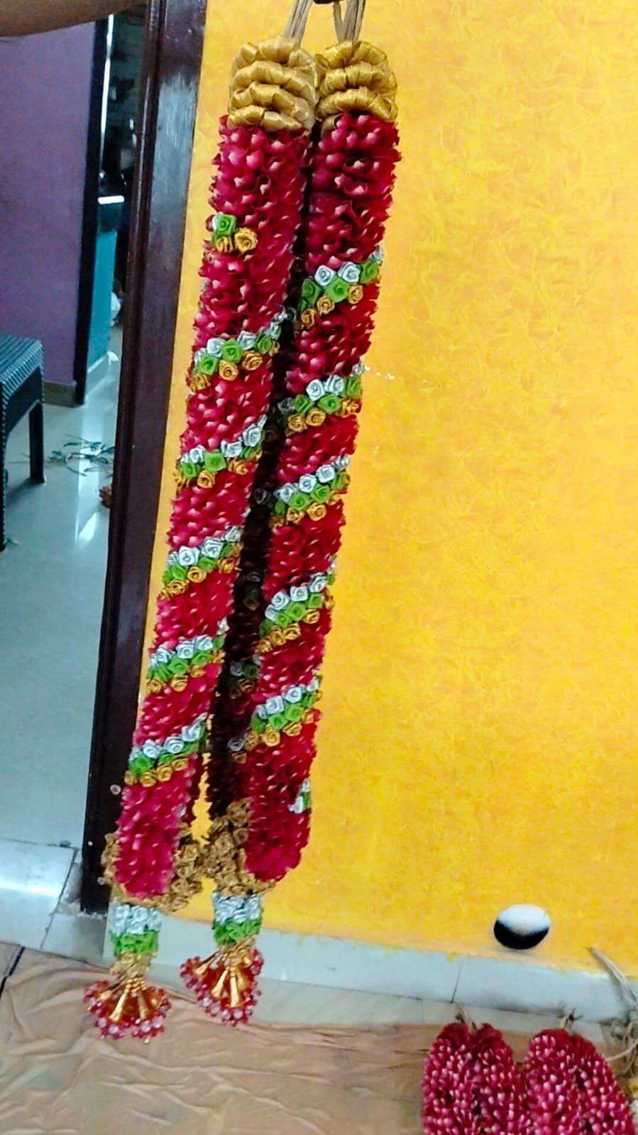 Pair of red garlands with green and white diagonal bands and gold tops, against a yellow wall.