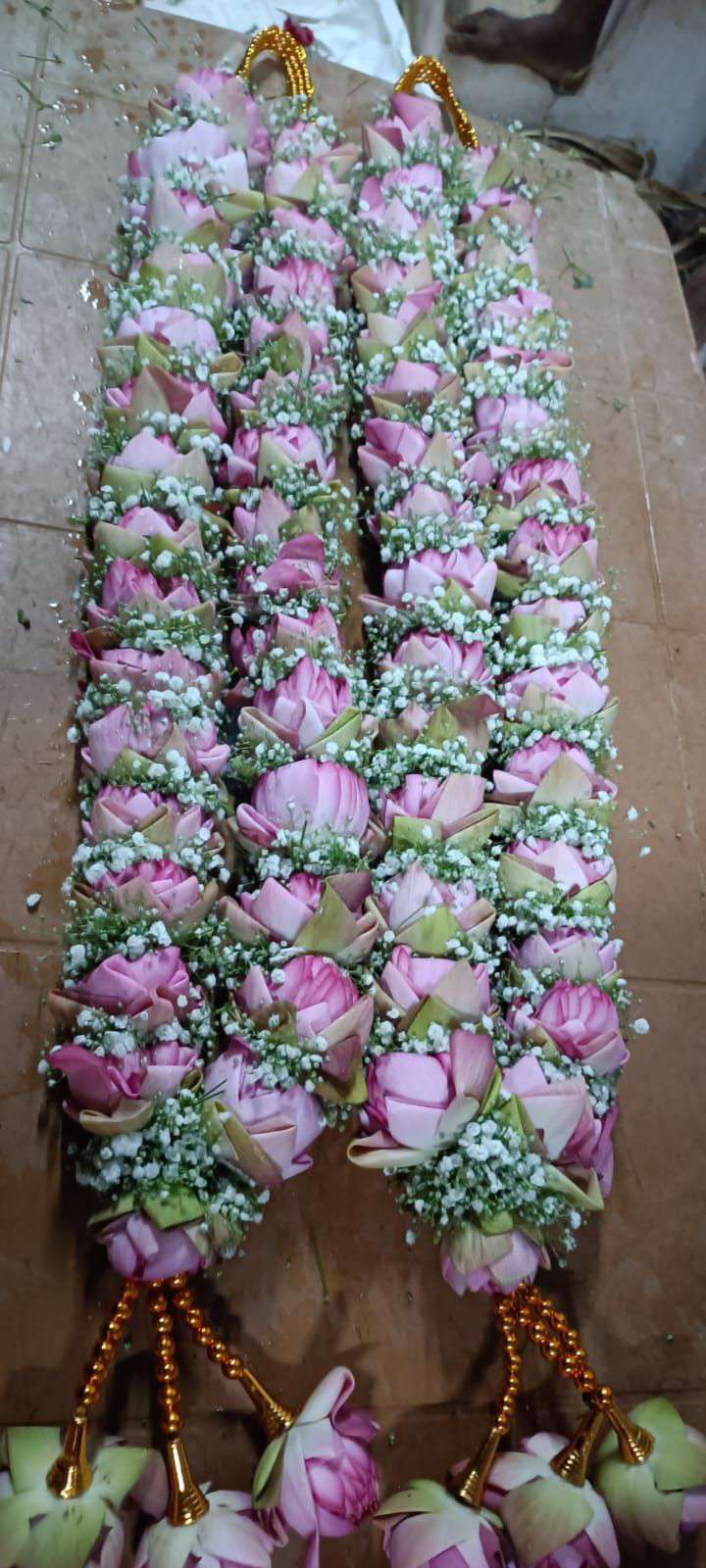 Pair of dense pink lotus and baby's breath garlands with gold bead tassels of lotus, laid flat.